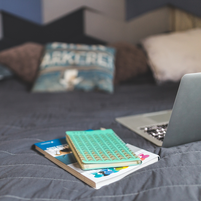 Notebooks and laptop on a bed