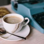 Close up of cup of coffee with a saucer typewriter on a desk