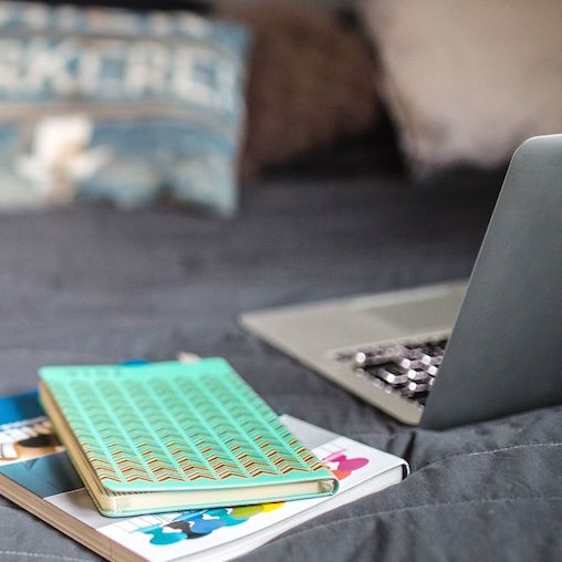 Notebooks and a laptop on a bed