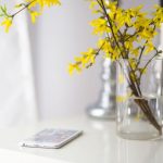 Forsythia in a glass vase and cell phone on a table