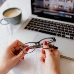 Woman holding a pair of glasses in front of a laptop
