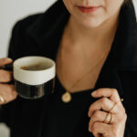 Woman holding a cup of coffee and wearing a gold necklace and rings