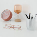 Clock, hourglass, glasses, and pen cup on a desk